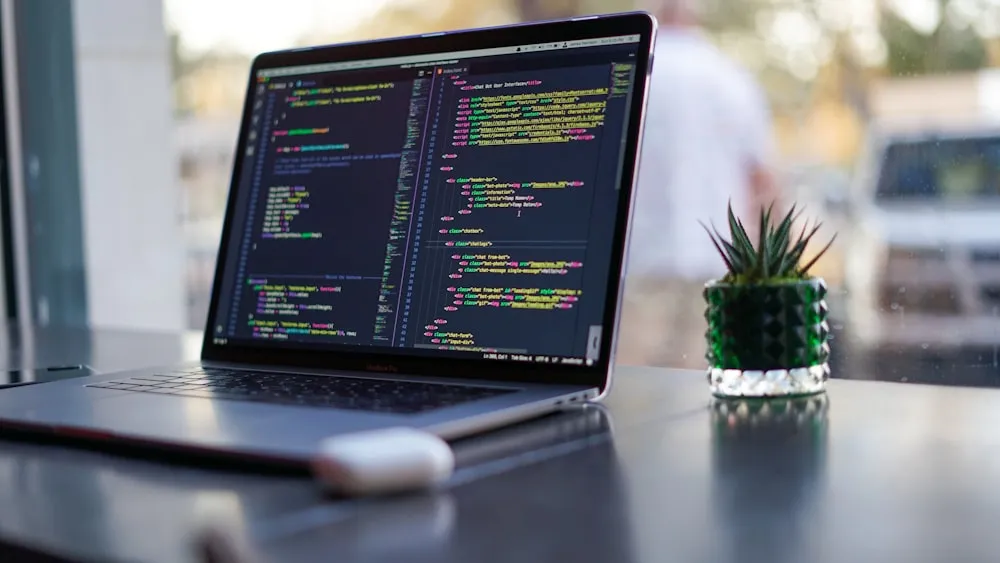 A laptop showing code beside a notebook and plant
