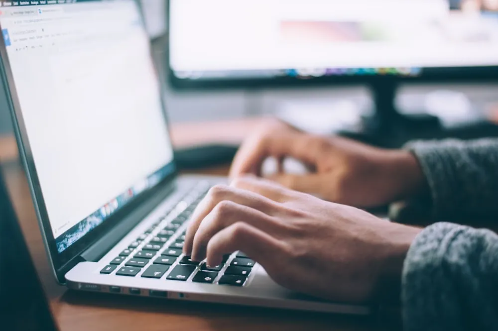 Writing at a laptop beside a monitor