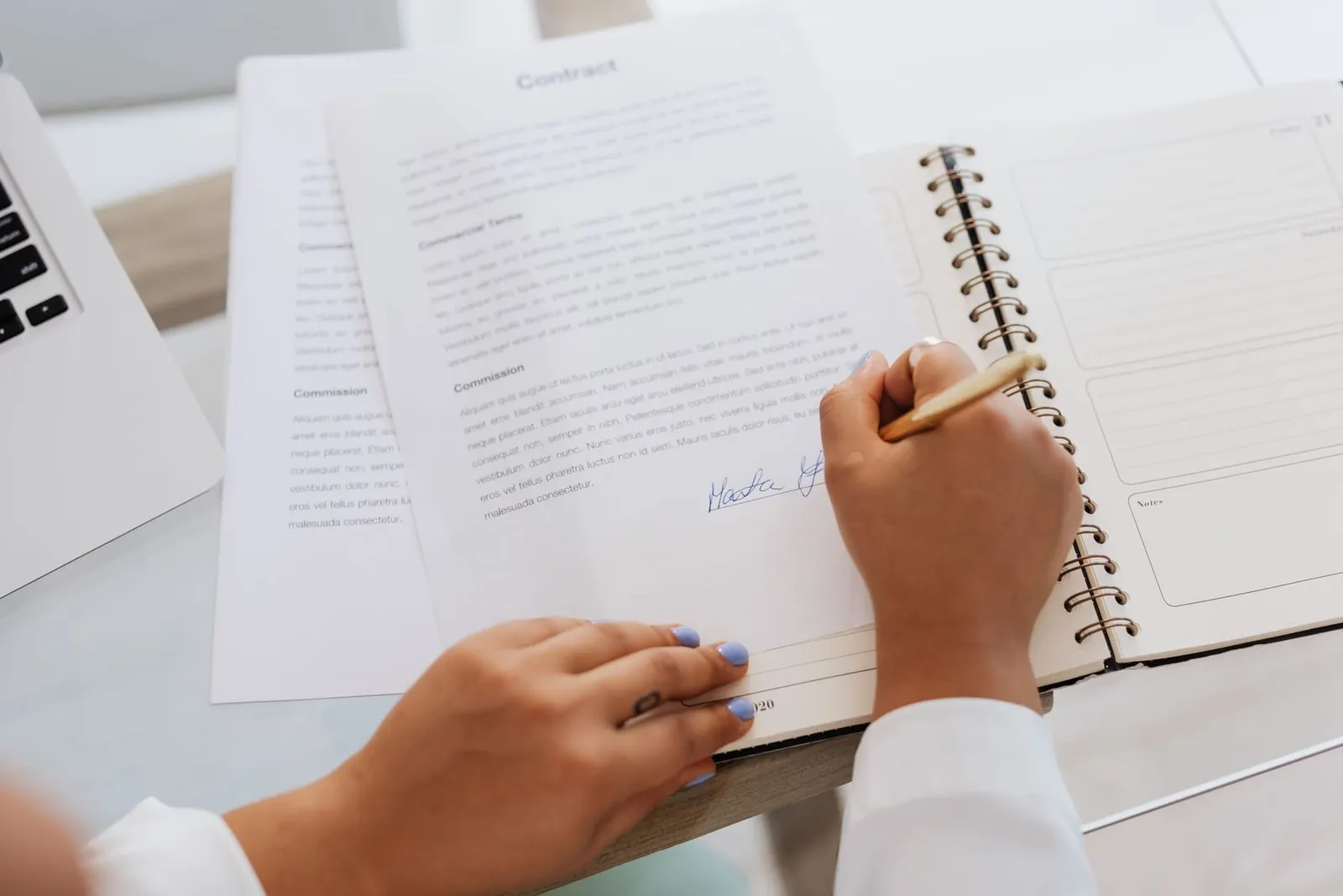 Hands filling in a printed form at a desk beside a notebook
